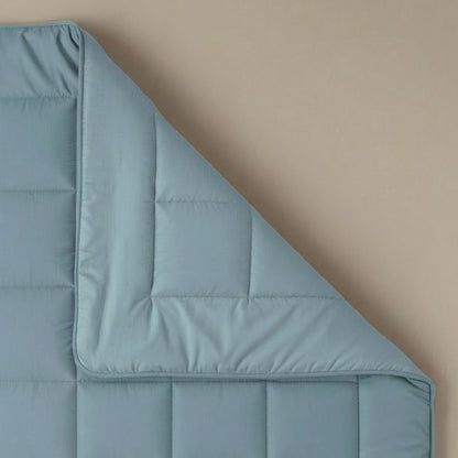 Het Zelesta Pure Uni Dekbed in sereen blauw, een lichtblauw katoenen dekbed, ligt netjes gevouwen op een beige achtergrond en biedt ademend slaapcomfort.