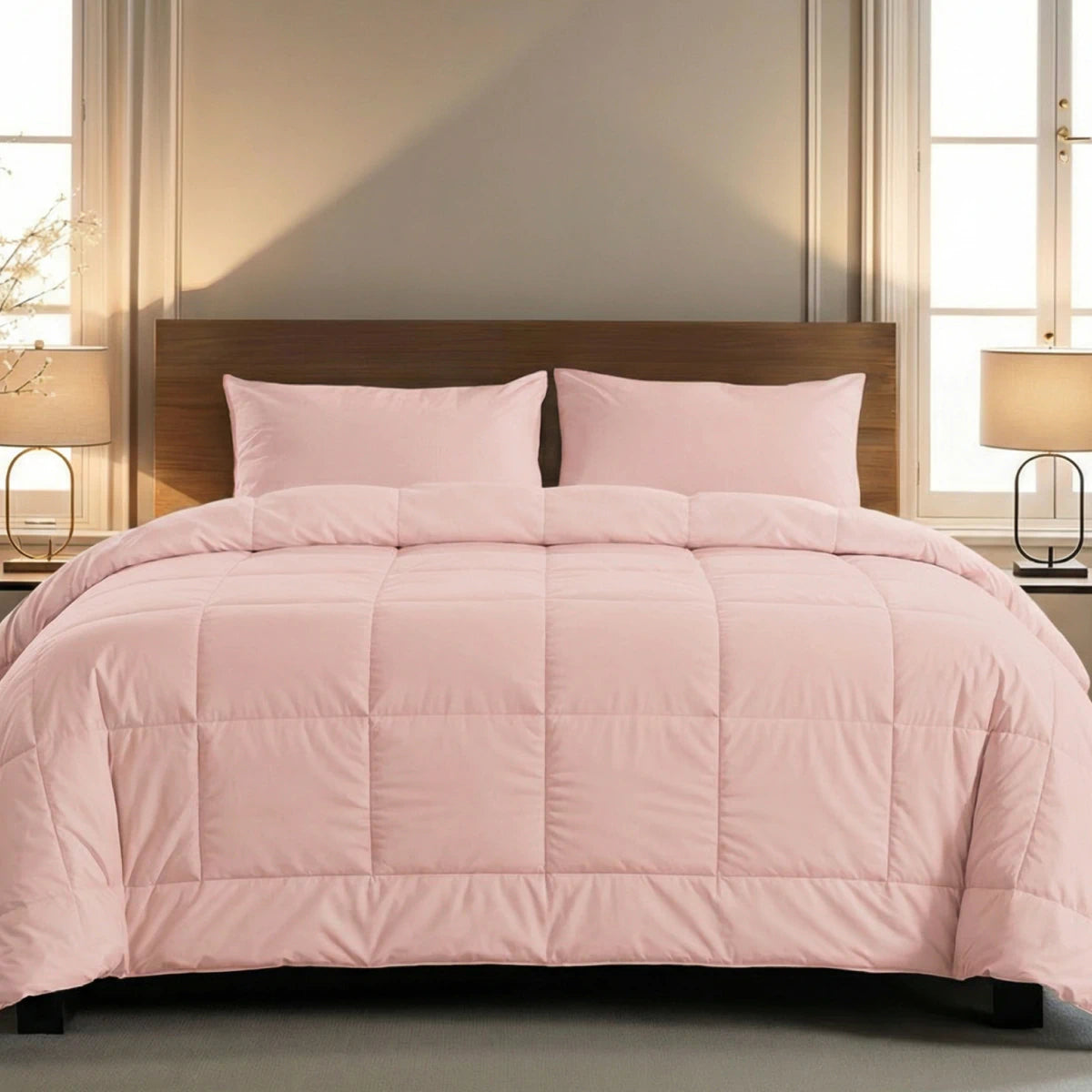 Een netjes opgemaakt bed met het Zelesta Pure Uni Dekbed in zacht roze en twee bijpassende kussens, geplaatst tussen twee ramen met nachtkastjes en lampen, biedt een ademend slaapcomfort.