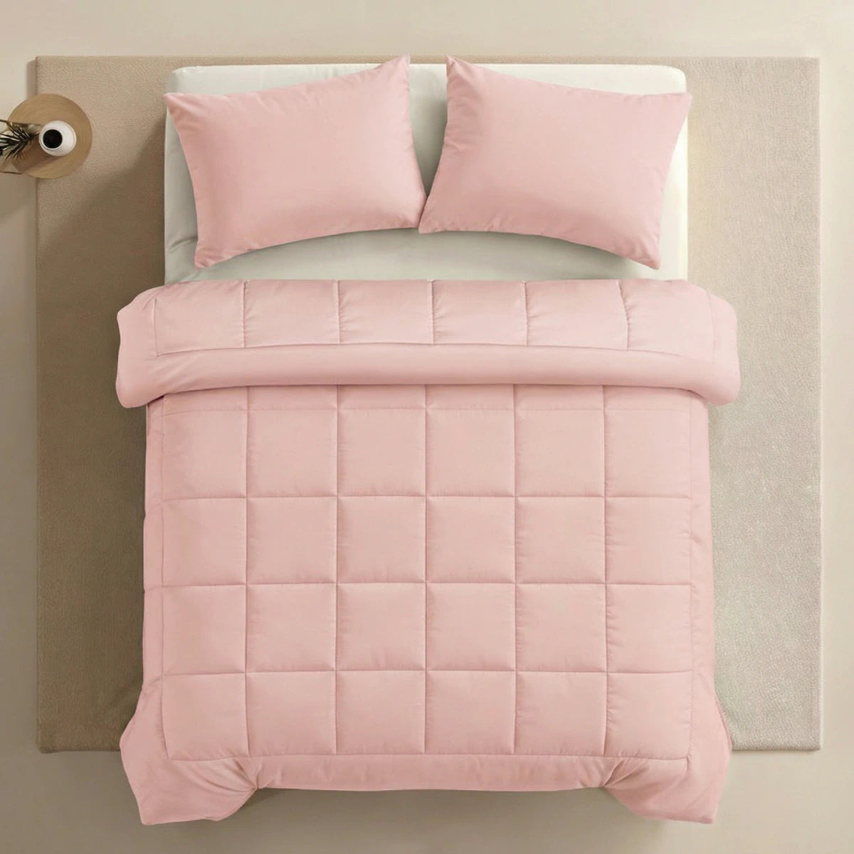 Een netjes opgemaakt bed met het Zelesta Pure Uni Dekbed in zacht roze en twee bijpassende kussens op een beige ondergrond, van bovenaf gezien - perfect voor ademend slaapcomfort.