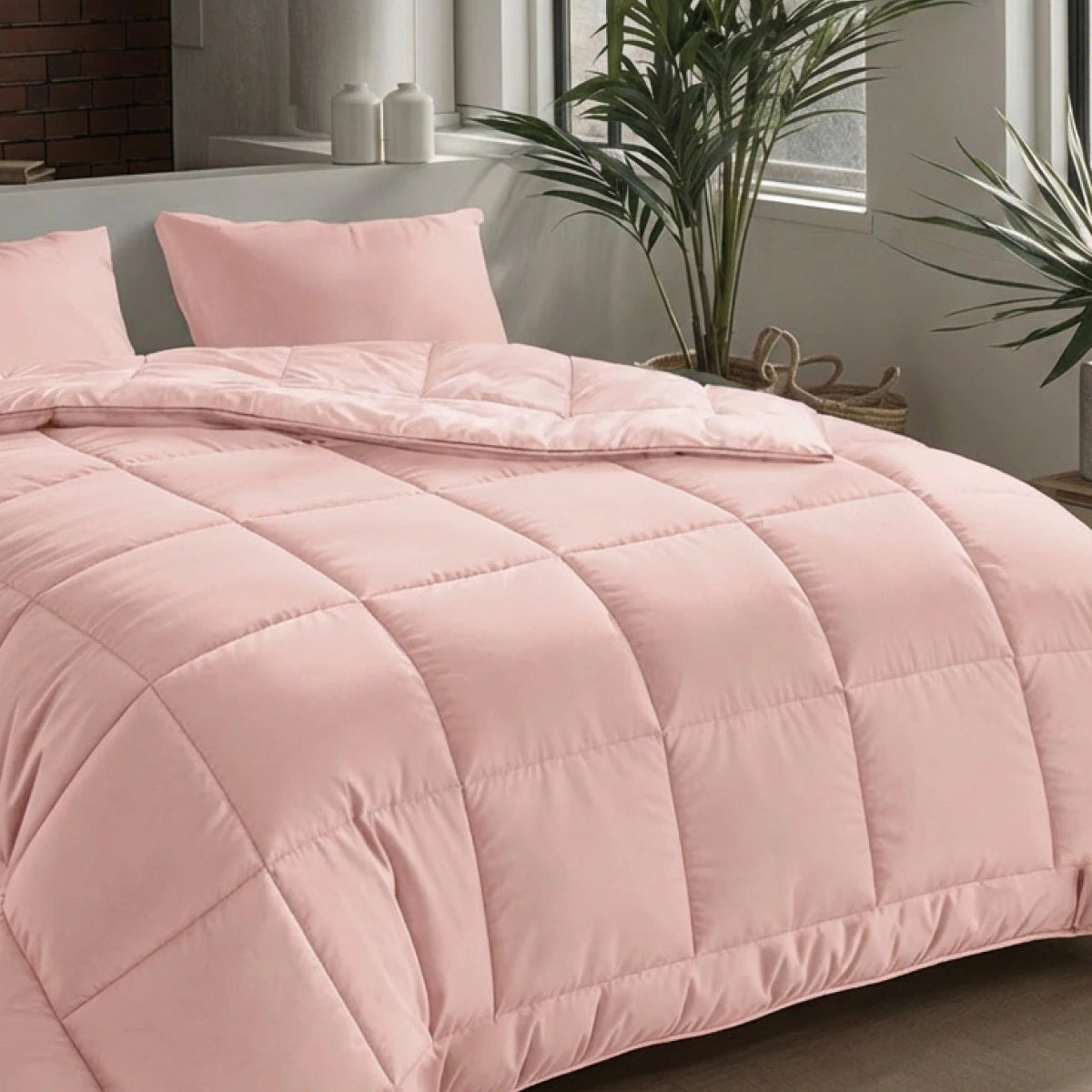 Een netjes opgemaakt bed met het Zelesta Pure Uni Dekbed in zacht roze met bijpassende kussens, bij een raam versierd met groene planten en wit decor voor een ademend slaapcomfort.