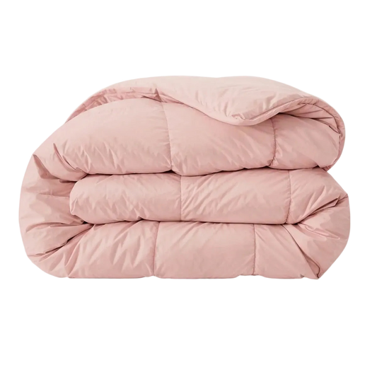 Het Zelesta Pure Uni Dekbed in zacht roze is een gevouwen, lichtroze katoenen dekbed met zichtbare stiksels op een effen witte ondergrond, dat een ademend slaapcomfort biedt.