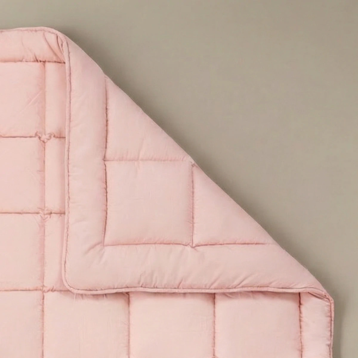 Het Zelesta Pure Uni Dekbed in zacht roze, gemaakt van katoen met vierkant stiksel, staat op een neutrale achtergrond met een omgeslagen hoek voor ademend slaapcomfort.