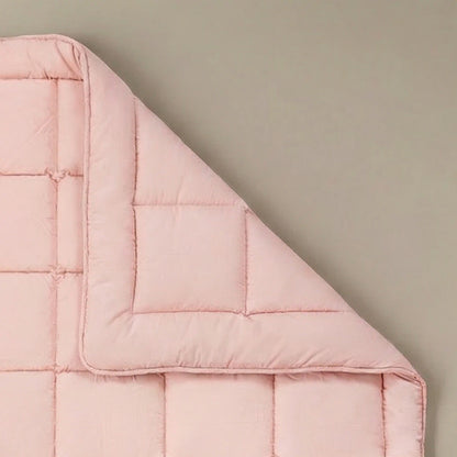 Het Zelesta Pure Uni Dekbed in zacht roze, gemaakt van katoen met vierkant stiksel, staat op een neutrale achtergrond met een omgeslagen hoek voor ademend slaapcomfort.