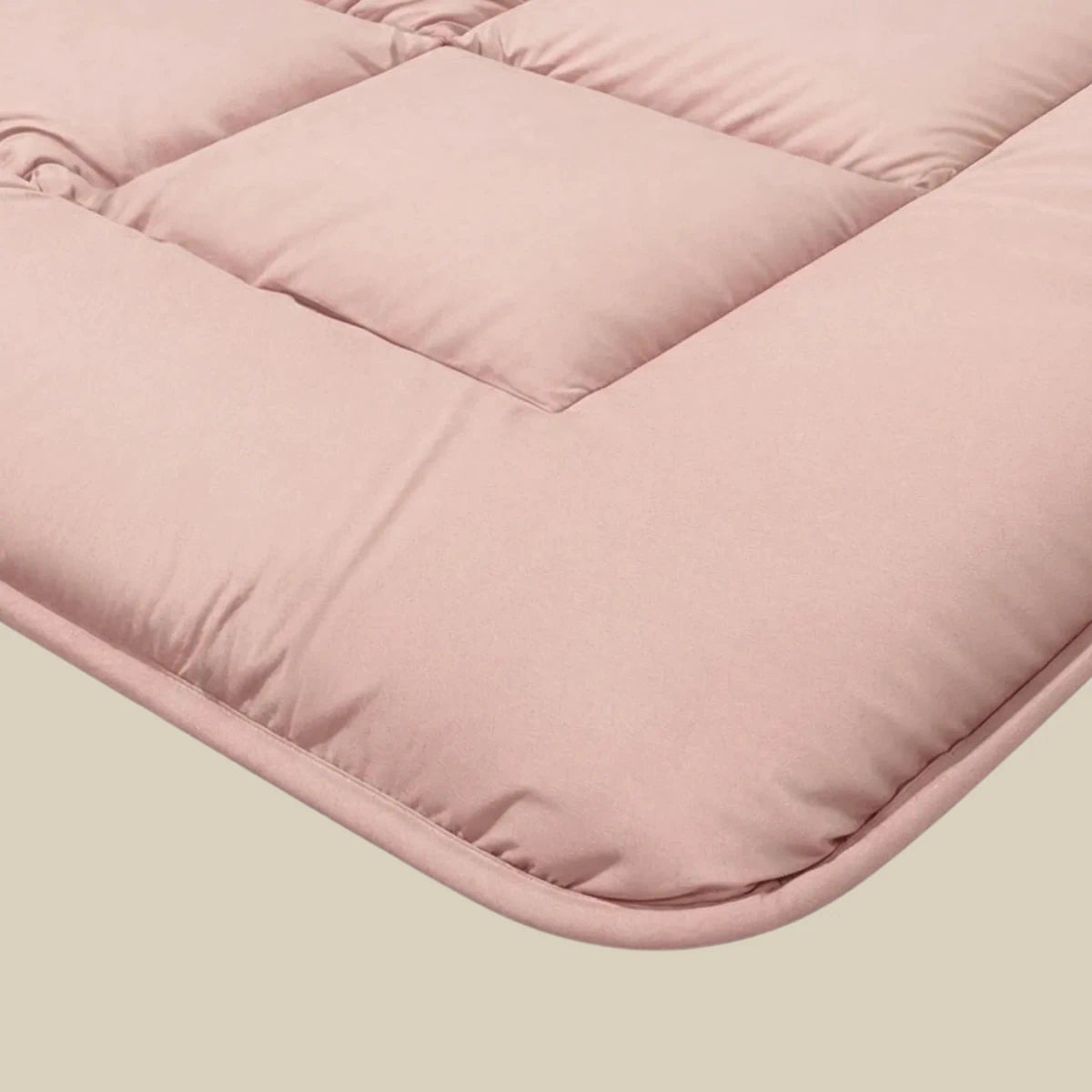 Close-up van het Zelesta Pure Uni Dekbed in zacht roze, met een gewatteerde, gedempte textuur en vierkante stiksels voor een ademend slaapcomfort en het knusse gevoel van een duurzaam dekbed op een neutrale achtergrond.