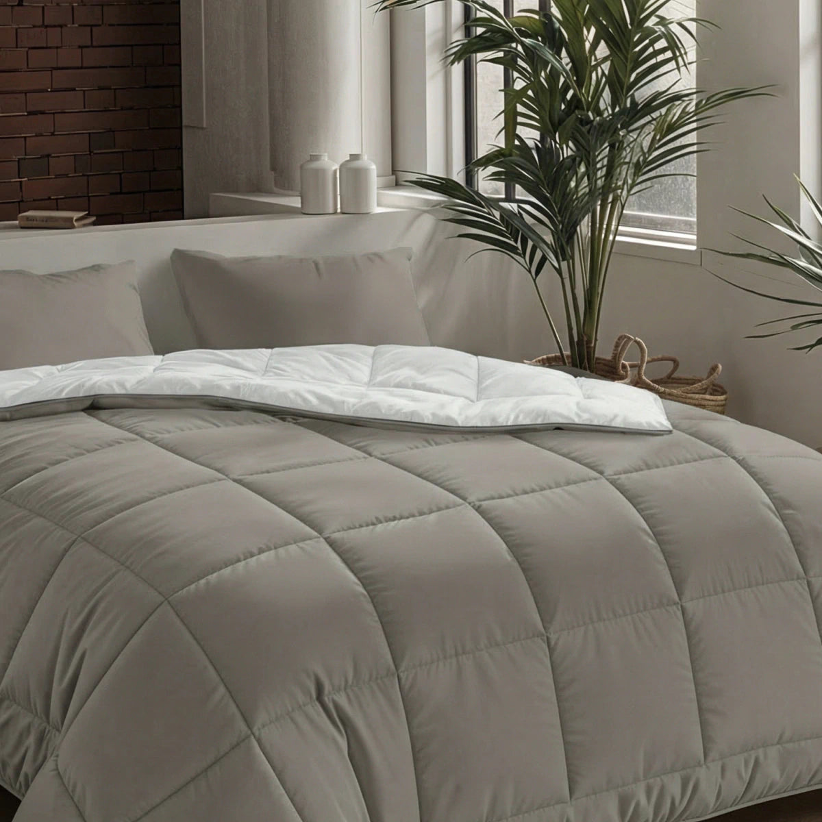 Een netjes opgemaakt bed met het Zelesta Pure Uni Dekbed - Antraciet Grijs in een moderne slaapkamer, omringd door potplanten en een raam met natuurlijk licht voor een ademend slaapcomfort.