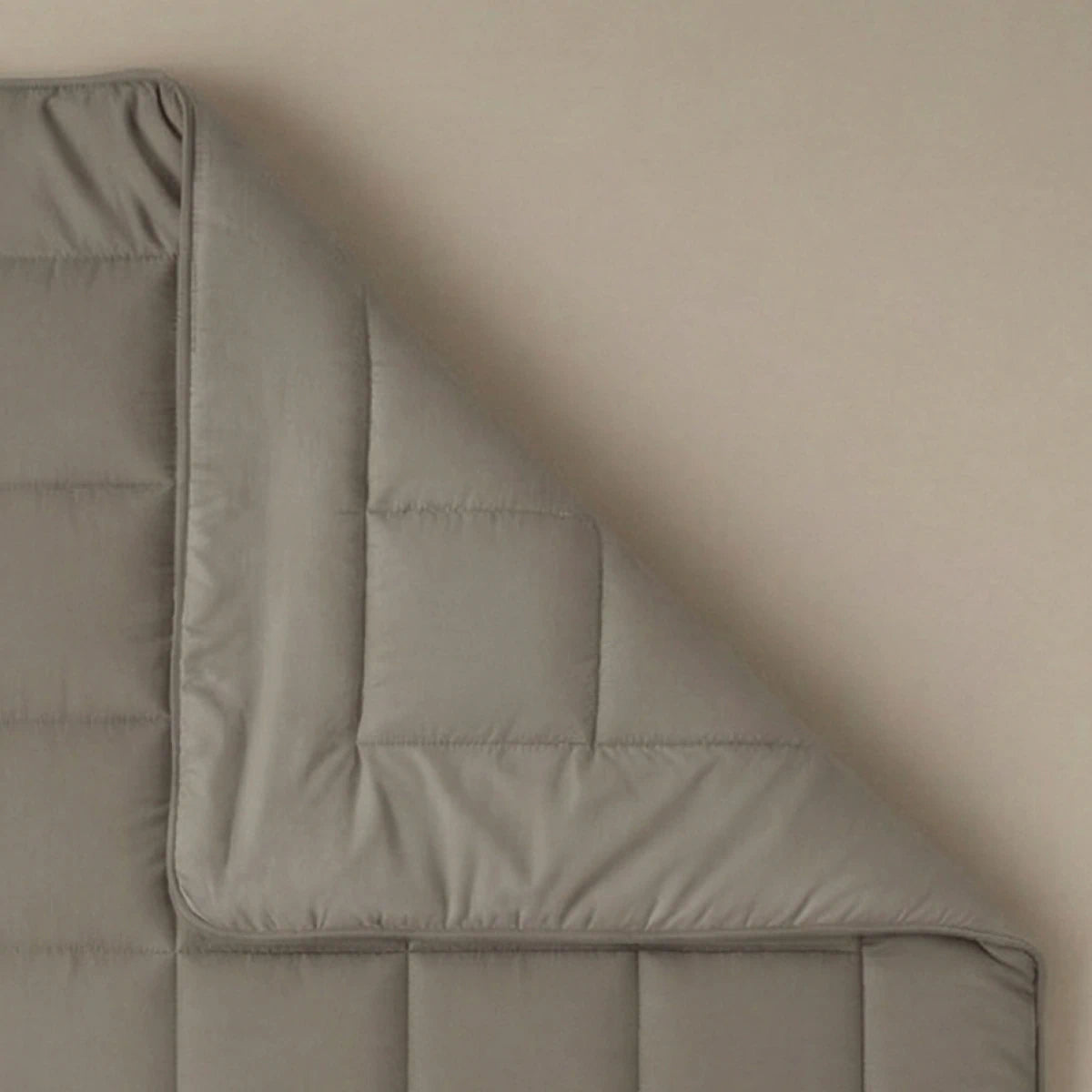 Een close-up van een hoek van het Zelesta Pure Uni Dekbed - Antraciet Grijs, een grijs gewatteerd dekbed, getoond tegen een effen achtergrond voor ademend slaapcomfort.