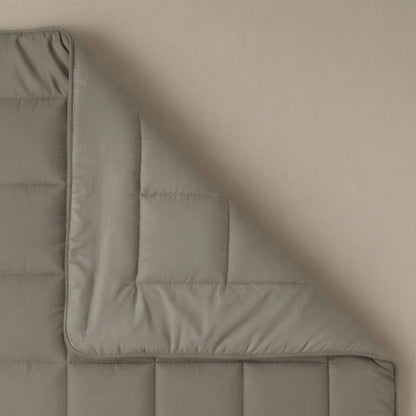 Een close-up van een hoek van het Zelesta Pure Uni Dekbed - Antraciet Grijs, een grijs gewatteerd dekbed, getoond tegen een effen achtergrond voor ademend slaapcomfort.