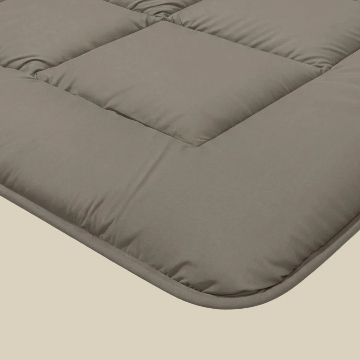 Close-up van een grijze, gewatteerde matrasopleg met gestikte vierkanten en afgeronde hoeken, ontworpen voor ademend slaapcomfort - perfect in combinatie met het Zelesta Pure Uni Dekbed - Antraciet Grijs.
